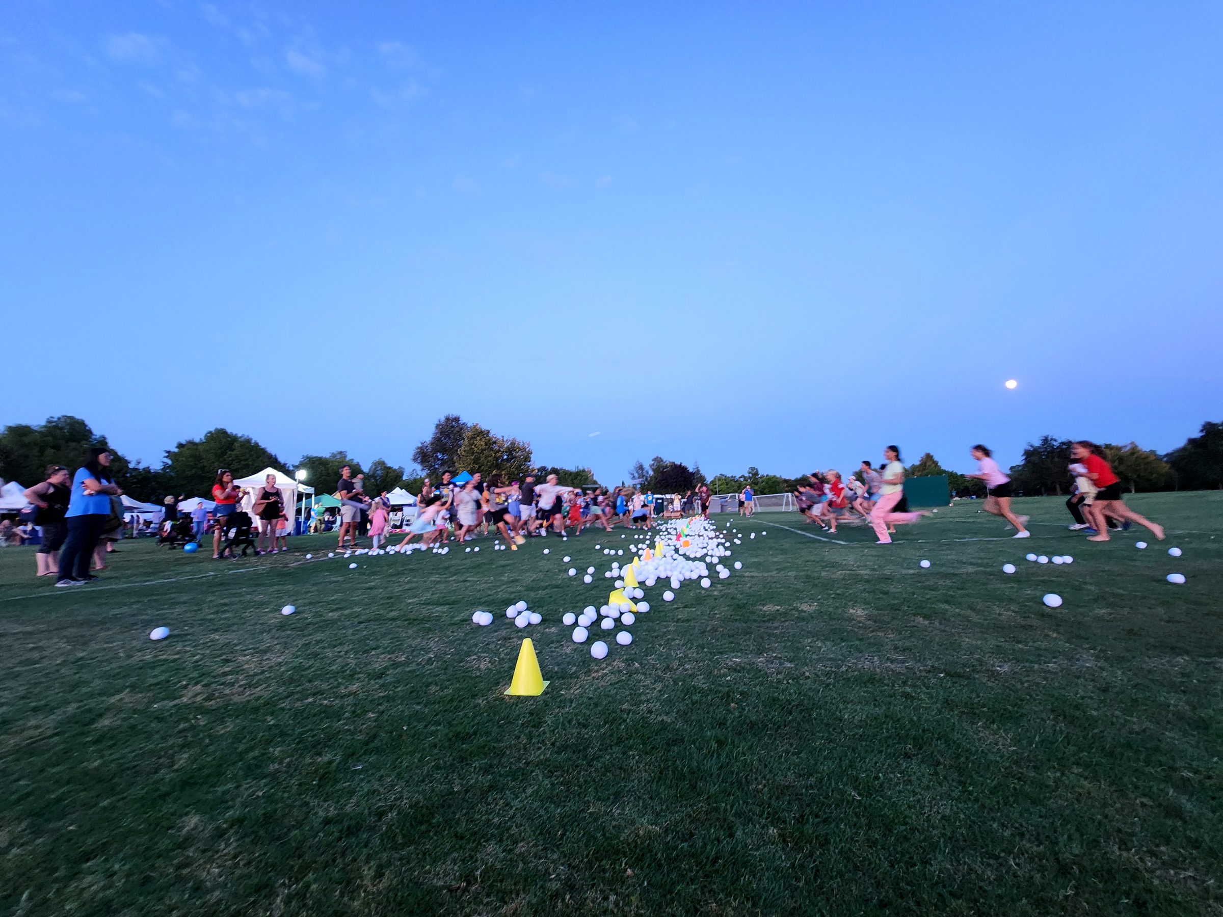 Hundreds of families and kids playing a giant glow-ball game together at dusk during the Davis Family Fun Fest