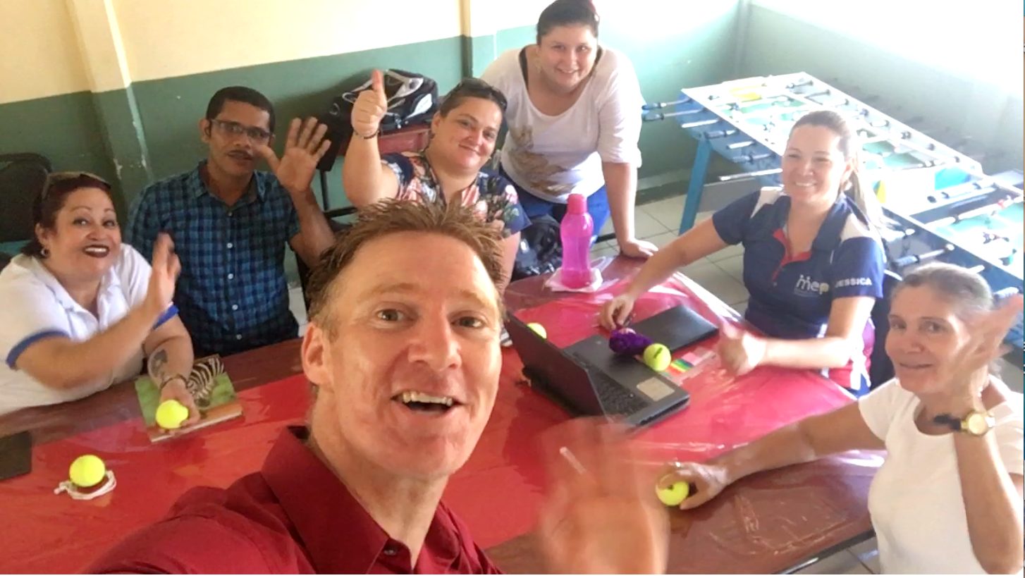 A teacher-training workshop gathered around a table abroad, learning the play-based happiness curriculum