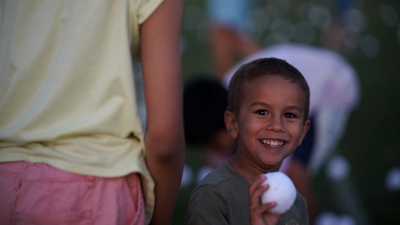 A young child beaming while holding a glow ball at dusk during the Family Fun Fest